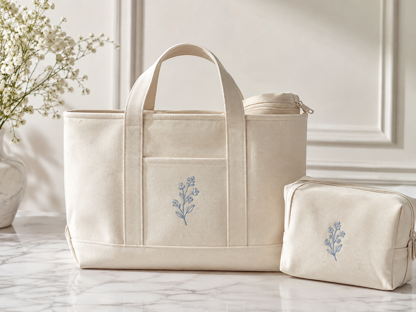 A cream canvas tote and matching zip pouch, each embroidered with a blue floral sprig